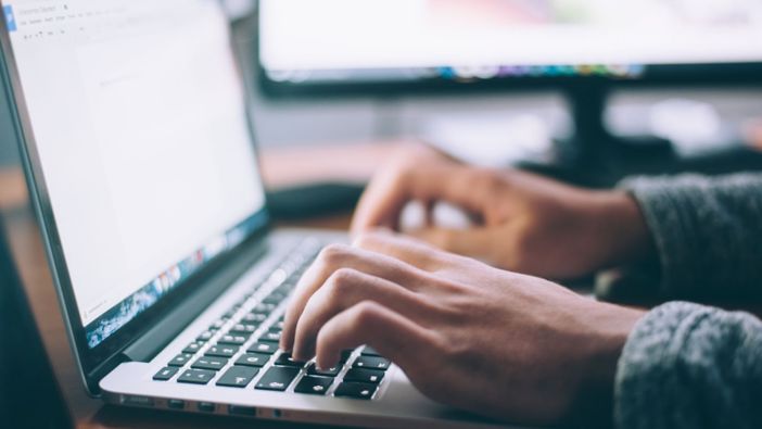 Nahaufnahme von Männerhänden, die auf der Tastatur eines Laptops schreiben.