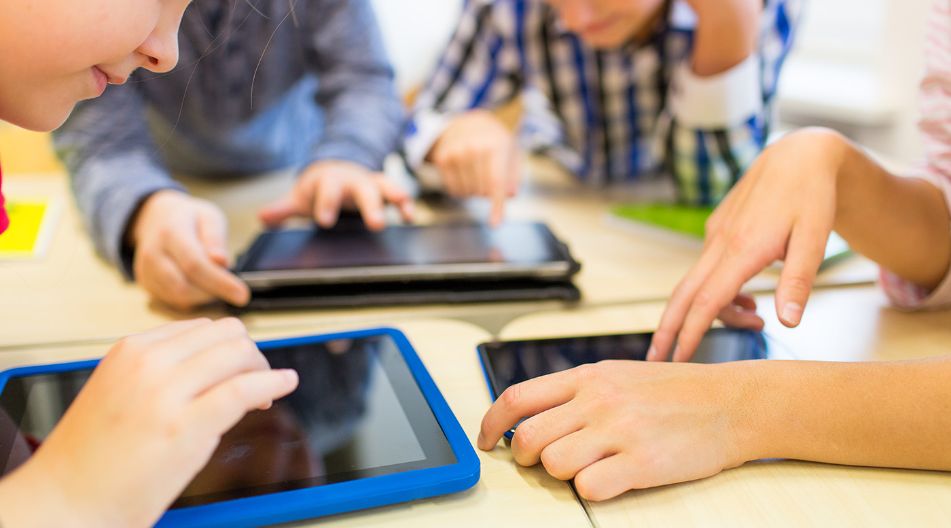 Mehrere Kinder sitzen an einem Tisch und bedienen Tablets mit ihren Fingern. Die Szene zeigt eine Lernumgebung mit moderner Technologie. Mehrere Kinder sitzen an einem Tisch und bedienen Tablets mit ihren Fingern. Die Szene zeigt eine Lernumgebung mit moderner Technologie.